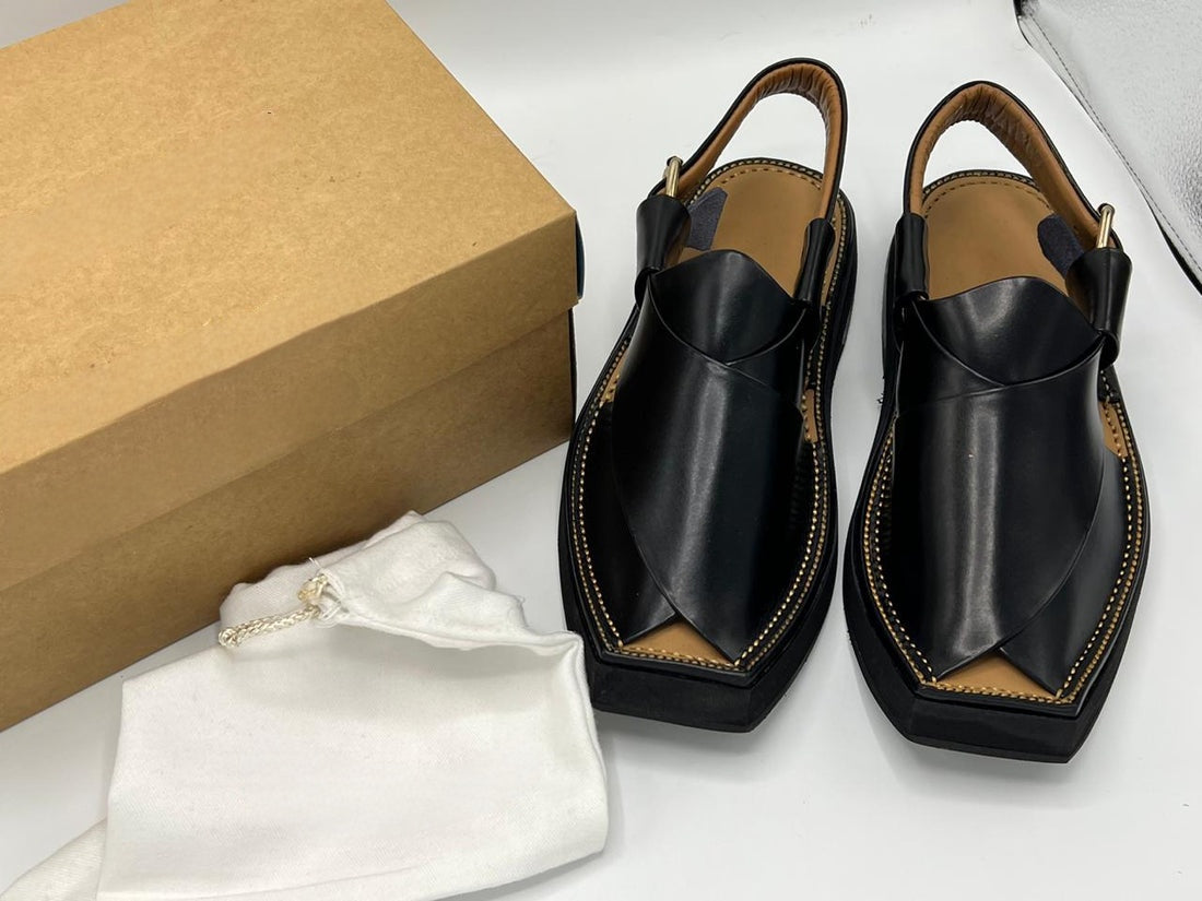 Pair of black leather sandals with tan interior next to a brown box on a white surface